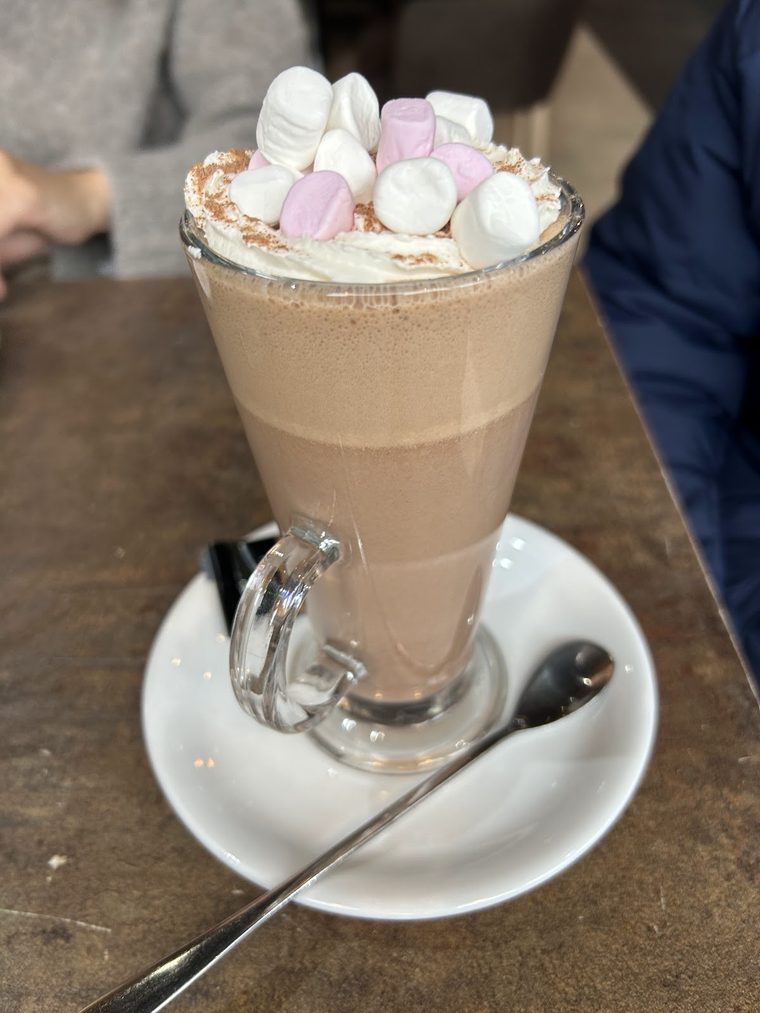 A tall glass mocha with whipped cream and marshmallows on a saucer
